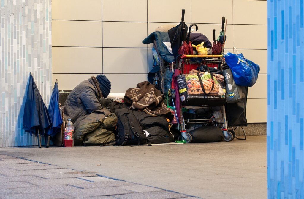 A homeless person is sitting next to a cart.